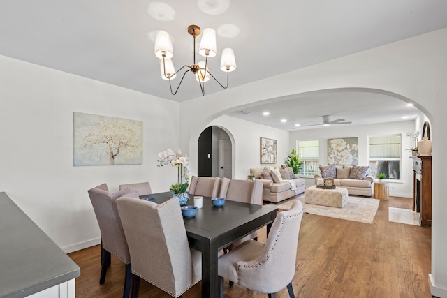dining area featuring ceiling fan with notable chandelier, arched walkways, recessed lighting, wood finished floors, and baseboards