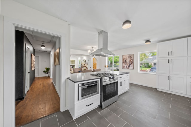 kitchen featuring dark tile patterned floors, baseboards, gas stove, white cabinetry, and island range hood