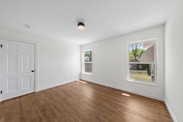 unfurnished room featuring baseboards, wood finished floors, and a healthy amount of sunlight
