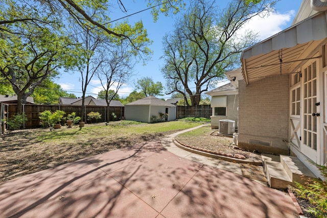 view of yard featuring an outbuilding, central AC, a fenced backyard, a patio, and french doors