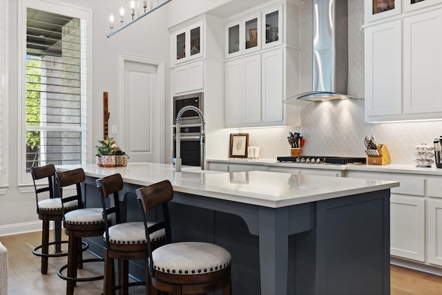 kitchen with wall chimney exhaust hood, a center island with sink, tasteful backsplash, a kitchen bar, and appliances with stainless steel finishes