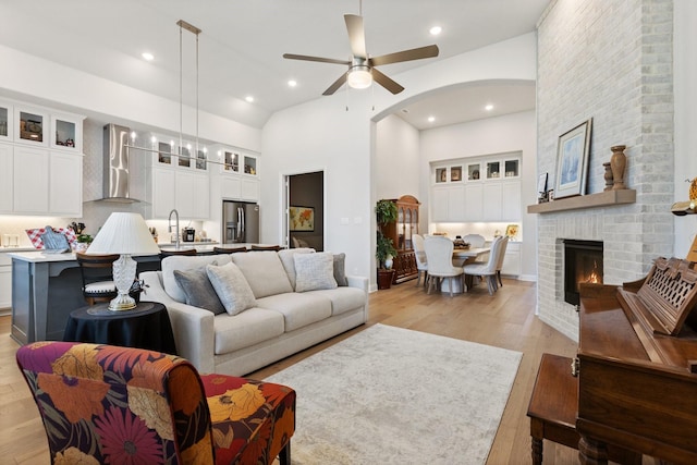 living room featuring a ceiling fan, light wood-style floors, arched walkways, a brick fireplace, and recessed lighting
