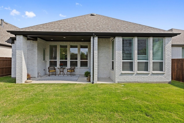 rear view of house with brick siding, fence, a patio area, and a shingled roof