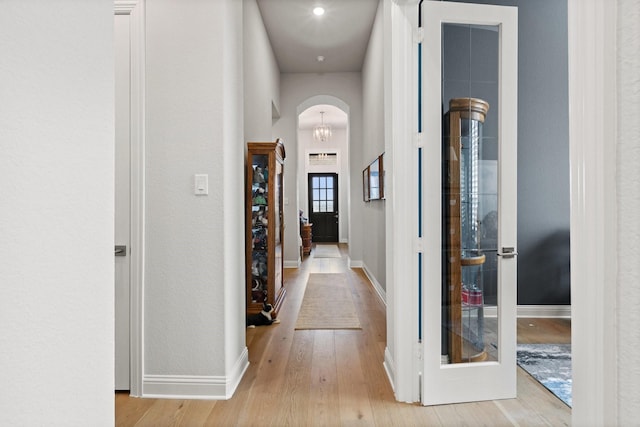 corridor with arched walkways, baseboards, wood finished floors, and an inviting chandelier