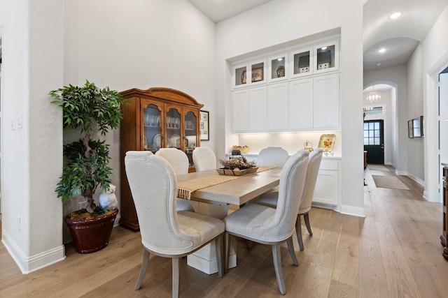 dining area featuring arched walkways, light wood-style flooring, a towering ceiling, and baseboards