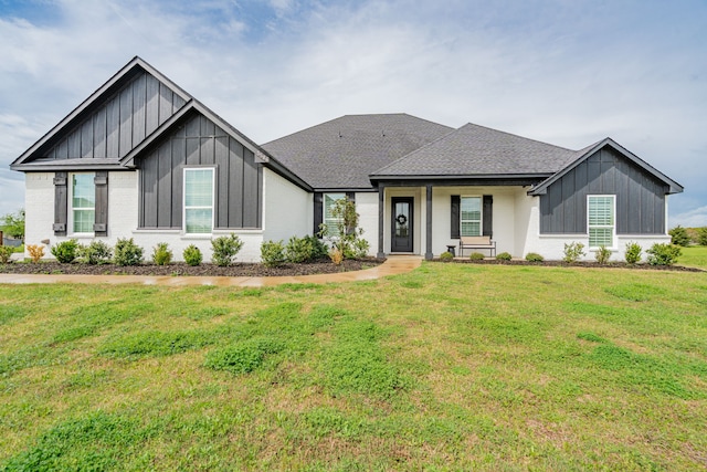 modern inspired farmhouse featuring board and batten siding, a front yard, a shingled roof, and brick siding
