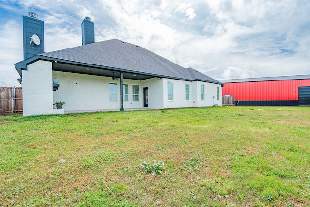 rear view of property featuring a yard, a chimney, fence, brick siding, and roof with shingles