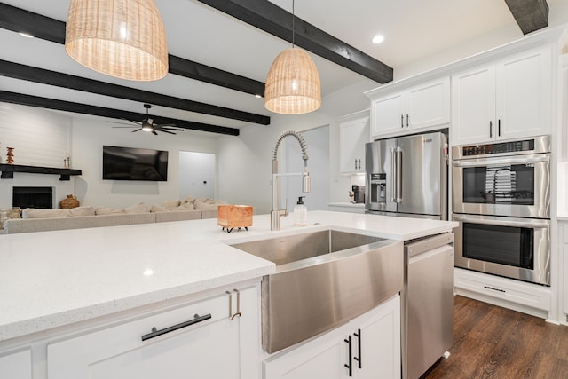 kitchen featuring a sink, ceiling fan, beamed ceiling, white cabinetry, and stainless steel appliances