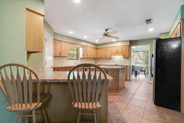 kitchen with a breakfast bar, a peninsula, freestanding refrigerator, a ceiling fan, and visible vents