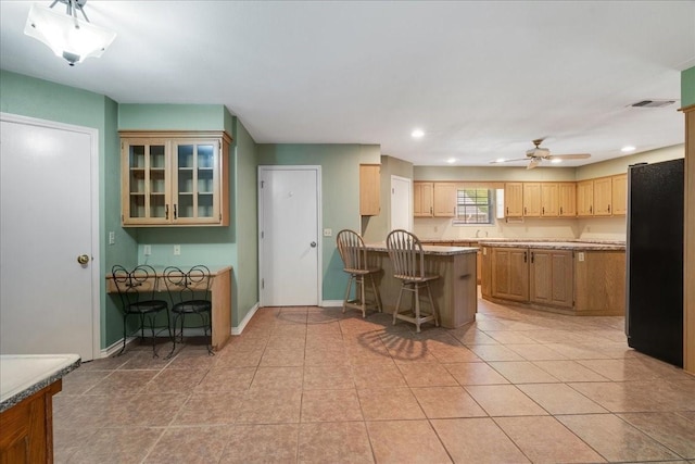 kitchen with freestanding refrigerator, a kitchen bar, a peninsula, a ceiling fan, and visible vents