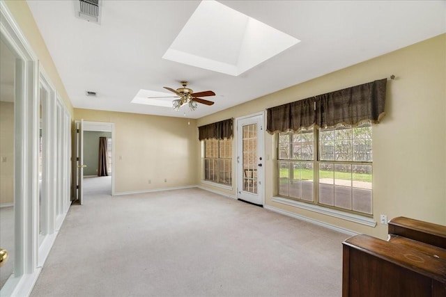 empty room with baseboards, a ceiling fan, visible vents, a skylight, and light colored carpet