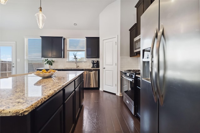 kitchen with light stone counters, dark wood-style floors, backsplash, stainless steel appliances, and hanging light fixtures