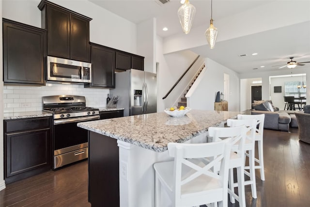 kitchen with a center island, appliances with stainless steel finishes, dark wood finished floors, decorative backsplash, and light stone counters