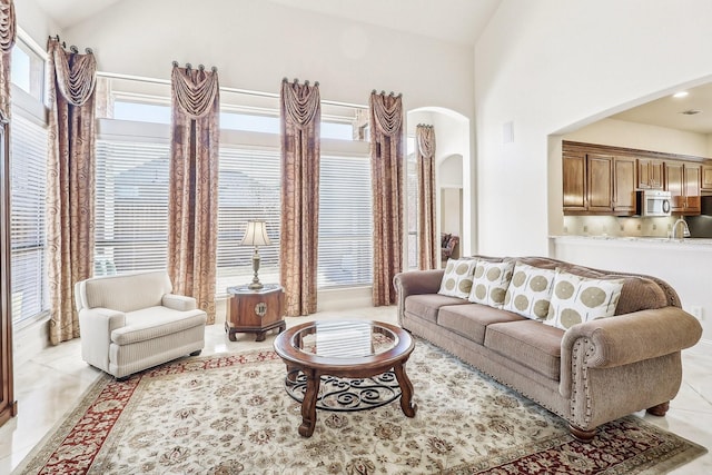 living area featuring arched walkways, high vaulted ceiling, and light tile patterned floors