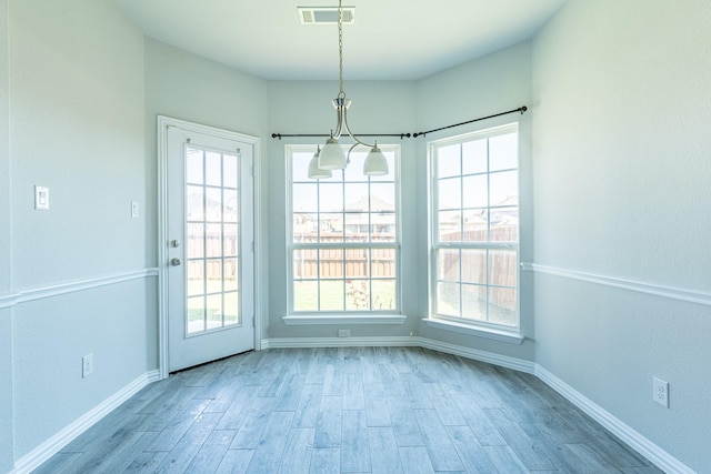 unfurnished dining area with wood finished floors, an inviting chandelier, baseboards, and visible vents