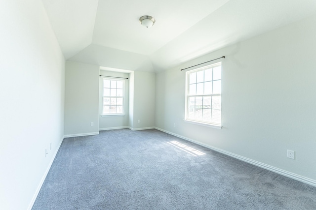 carpeted spare room featuring baseboards and vaulted ceiling