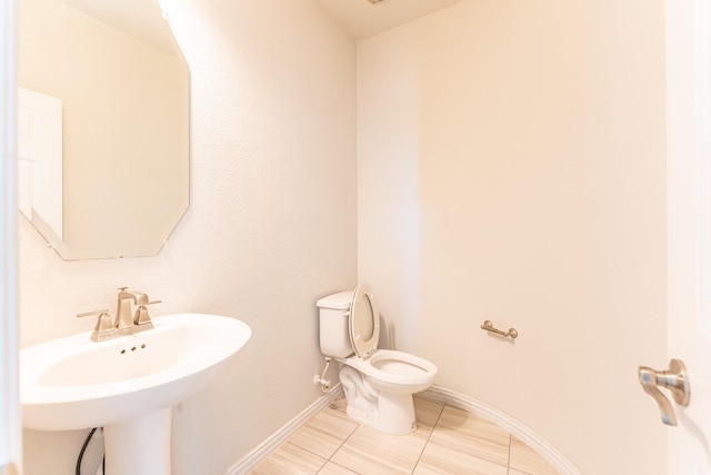 half bathroom featuring a sink, tile patterned floors, toilet, and baseboards