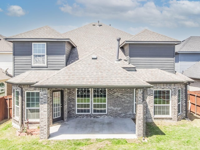 rear view of property with a lawn, roof with shingles, a patio area, fence, and brick siding