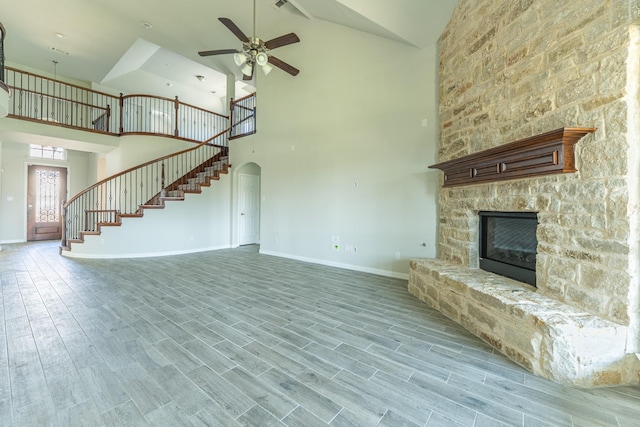 unfurnished living room featuring high vaulted ceiling, a fireplace, ceiling fan, stairs, and baseboards