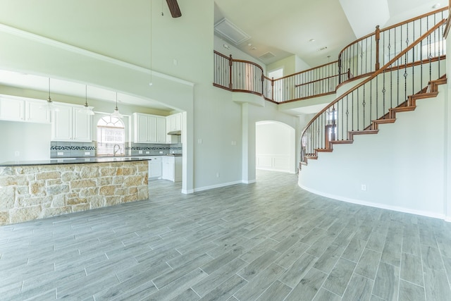 unfurnished living room featuring baseboards, arched walkways, light wood-style floors, a towering ceiling, and stairs