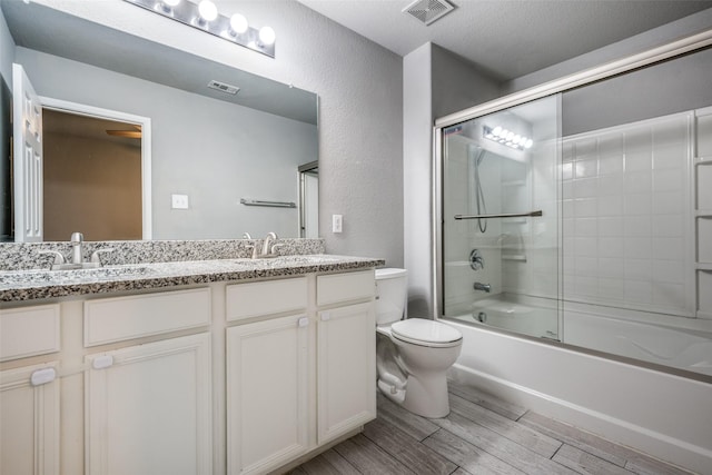 full bath featuring toilet, wood finish floors, a sink, and bath / shower combo with glass door