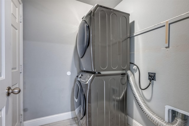 clothes washing area with laundry area, stacked washer and clothes dryer, and baseboards
