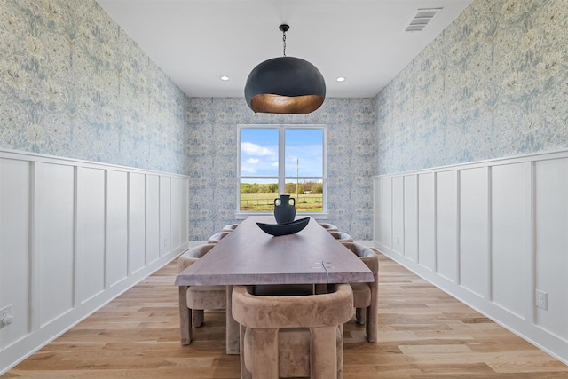 dining area featuring a decorative wall, wallpapered walls, wainscoting, light wood-style floors, and visible vents