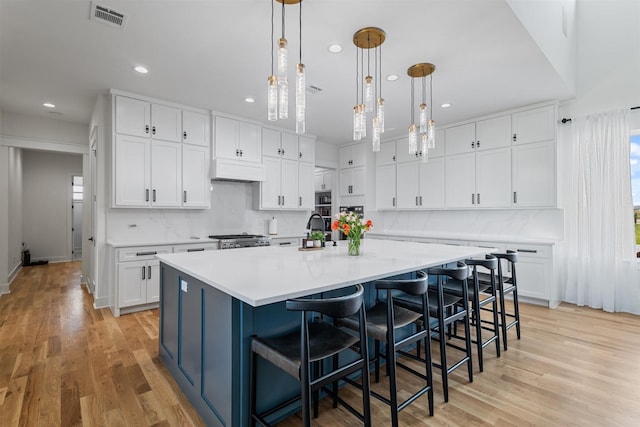 kitchen featuring a large island with sink, range, under cabinet range hood, visible vents, and recessed lighting