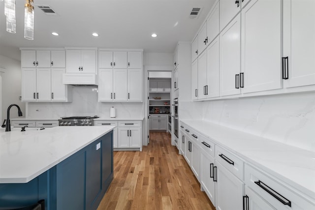 kitchen with white cabinetry, custom exhaust hood, range, and visible vents