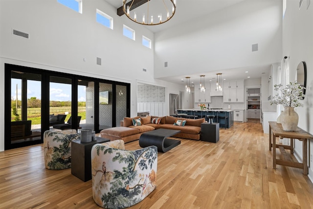 living area featuring a high ceiling, a notable chandelier, visible vents, and light wood-style flooring