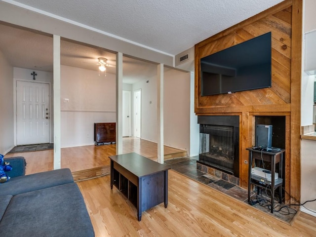 living area with a fireplace with flush hearth, a textured ceiling, a ceiling fan, visible vents, and wood finished floors