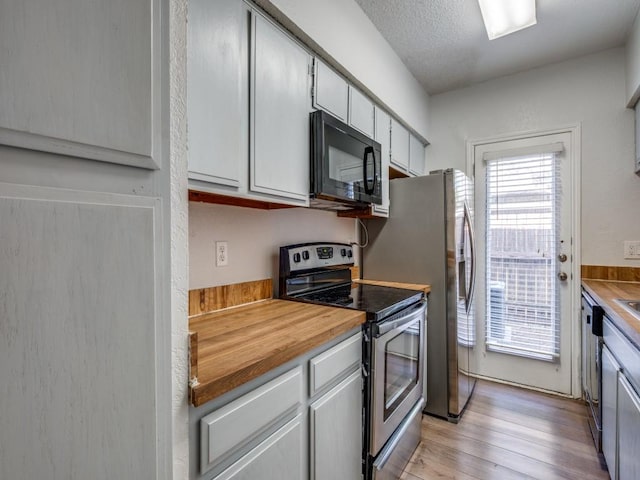 kitchen with stainless steel electric range, black microwave, wood counters, light wood-style floors, and dishwashing machine