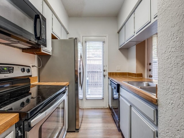 kitchen with wood counters, white cabinets, black appliances, light wood finished floors, and a sink