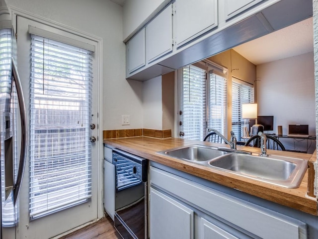 kitchen with butcher block countertops, light wood-type flooring, black dishwasher, white cabinets, and a sink