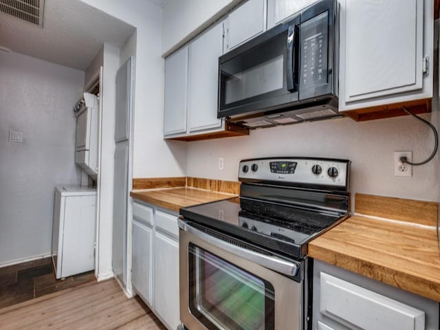 kitchen featuring stainless steel electric range oven, visible vents, wooden counters, stacked washer / drying machine, and black microwave