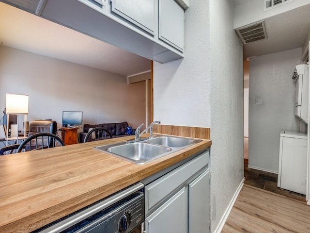 kitchen featuring light wood-style flooring, dishwashing machine, a sink, and visible vents