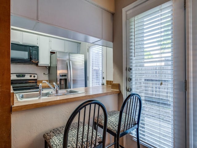 kitchen with a sink, white cabinets, a textured wall, and stainless steel appliances