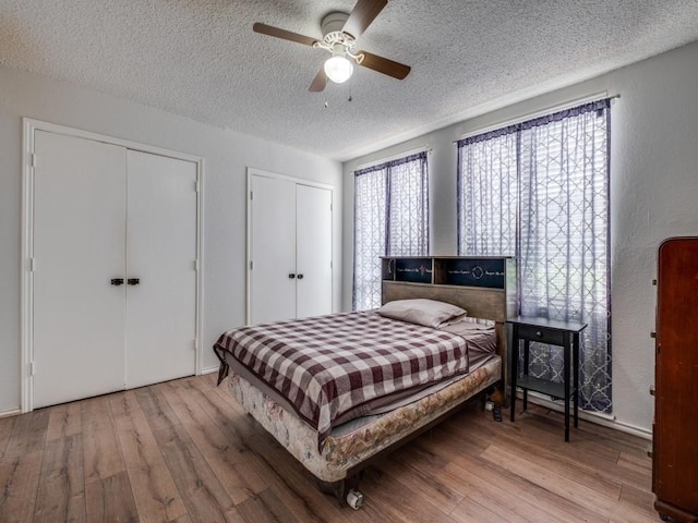 bedroom with a textured ceiling, multiple windows, multiple closets, and wood finished floors