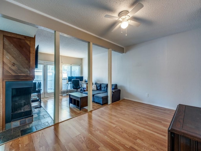 living area featuring a textured ceiling, wood finished floors, ceiling fan, and a fireplace