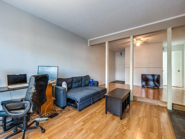 living area featuring light wood finished floors, a textured ceiling, and a ceiling fan