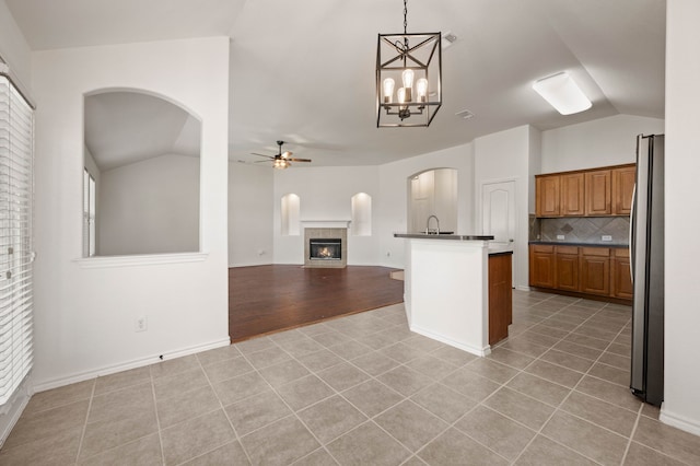 kitchen featuring ceiling fan with notable chandelier, light tile patterned floors, brown cabinetry, dark countertops, and lofted ceiling