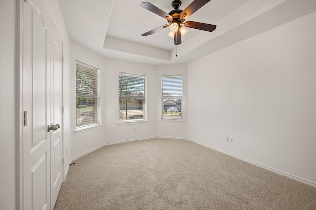 unfurnished room with light carpet, baseboards, a ceiling fan, and a raised ceiling