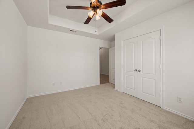 unfurnished bedroom featuring carpet, a closet, visible vents, a raised ceiling, and baseboards