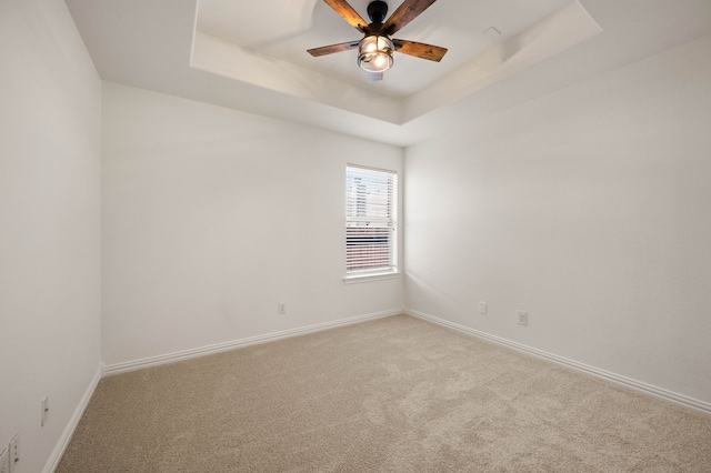 spare room featuring a raised ceiling, light colored carpet, ceiling fan, and baseboards