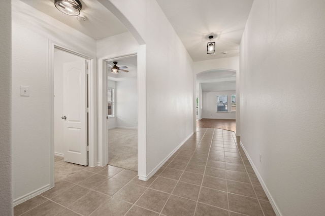 hall featuring arched walkways, a healthy amount of sunlight, and tile patterned flooring