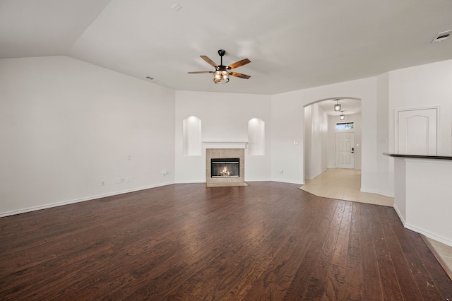 unfurnished living room with a tiled fireplace, visible vents, a ceiling fan, and wood finished floors