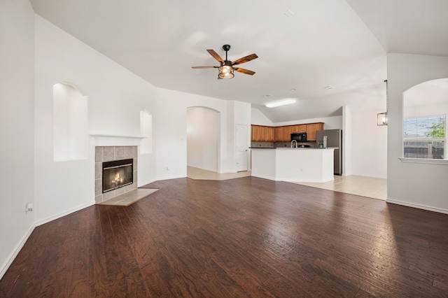 unfurnished living room featuring light wood-style floors, a ceiling fan, vaulted ceiling, a tile fireplace, and baseboards