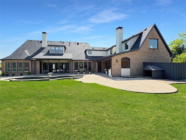 rear view of house featuring a chimney, a yard, a patio area, and brick siding
