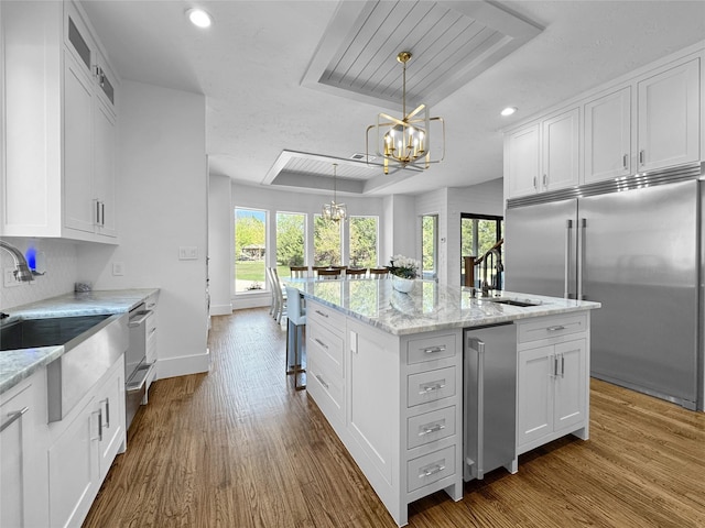 kitchen featuring white cabinets, a notable chandelier, a kitchen island with sink, and built in fridge