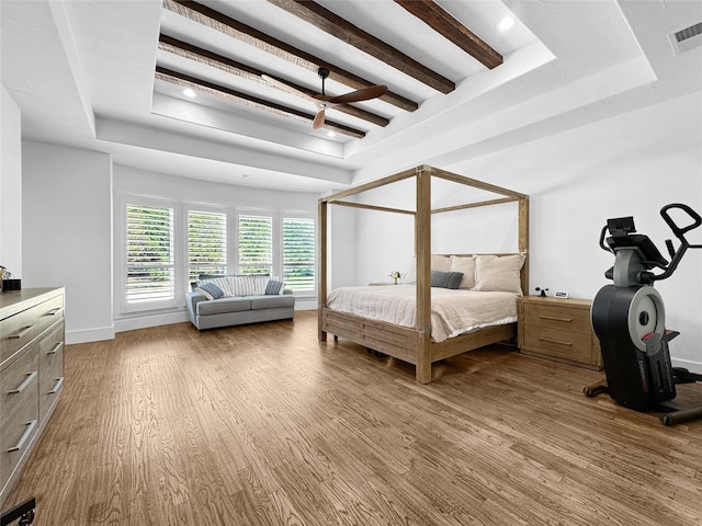 bedroom with a ceiling fan, a tray ceiling, wood finished floors, and visible vents